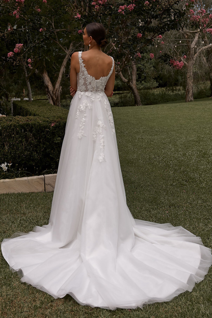 White wedding dress with intricate detailing with long train in a garden setting