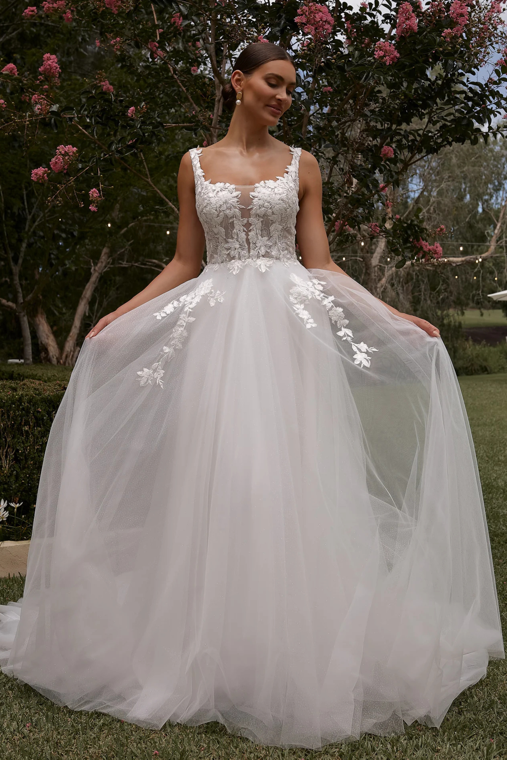 Bride in a white wedding dress with floral details standing outdoors.