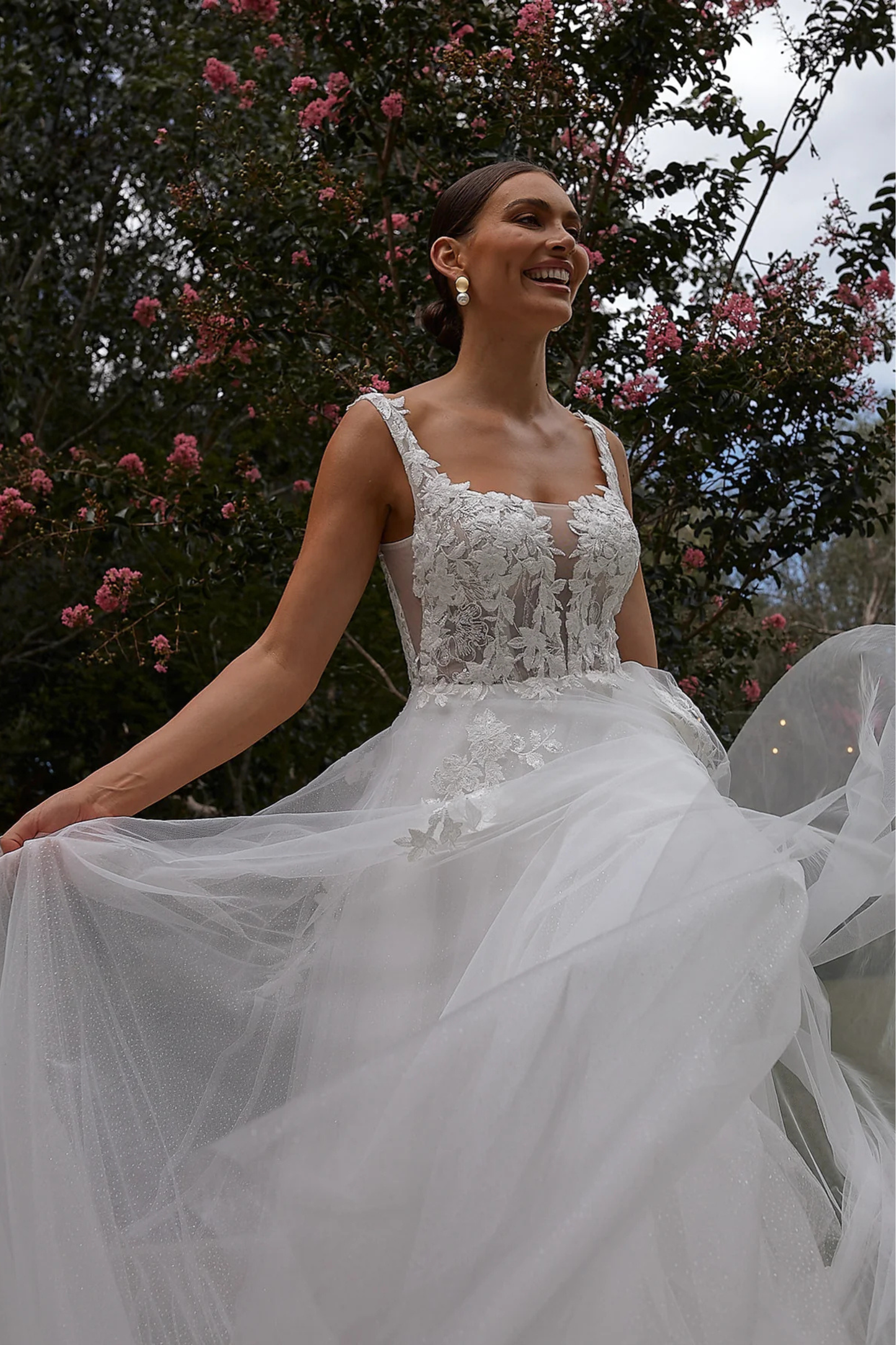 Bride in a white wedding dress standing outdoors with pink flowers in the background