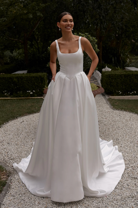 Woman in a white wedding dress standing outdoors with greenery in the background