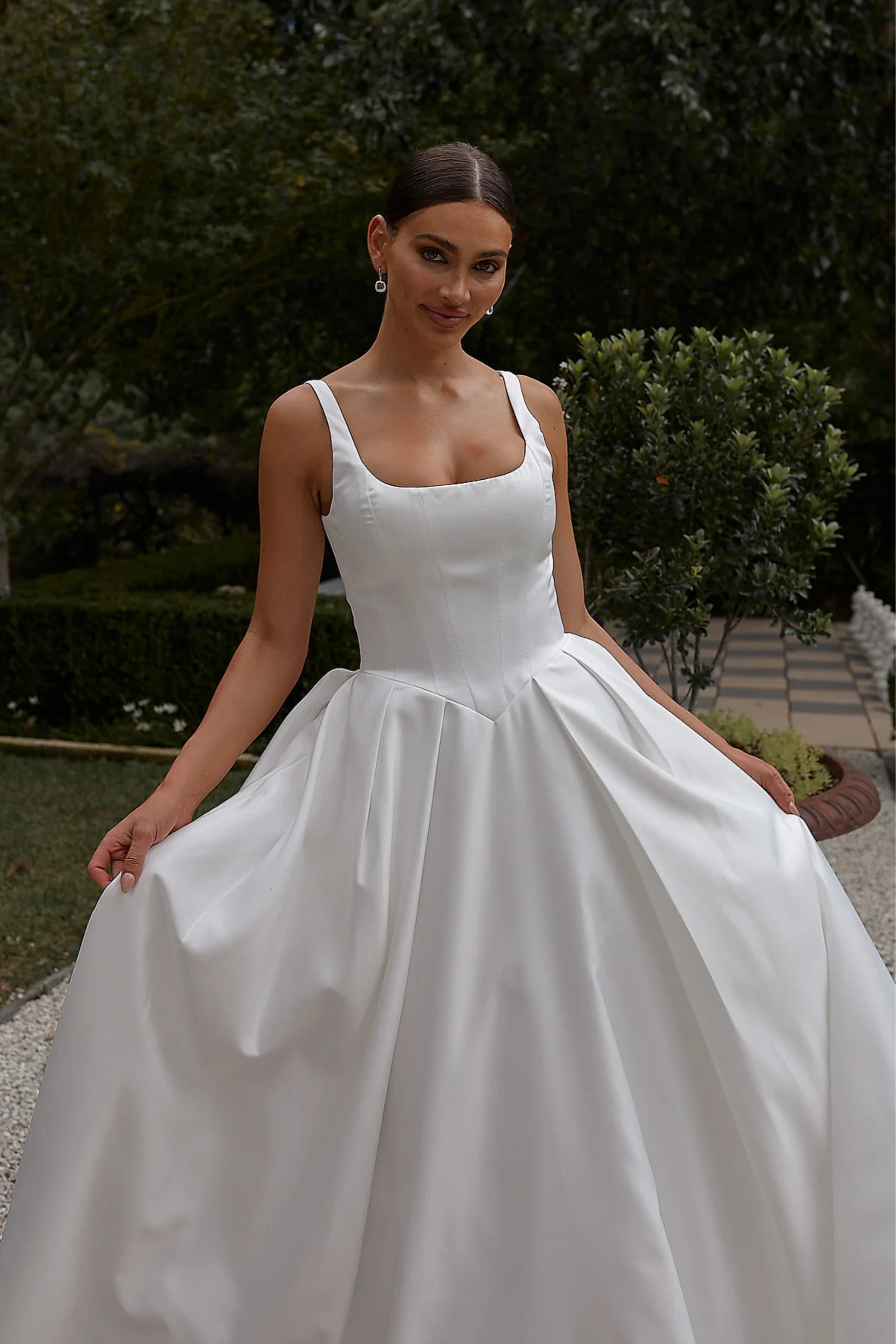 Woman wearing a white wedding dress outdoors with greenery in the background