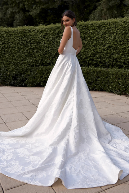 White wedding dress with a long train on a paved path with greenery in the background