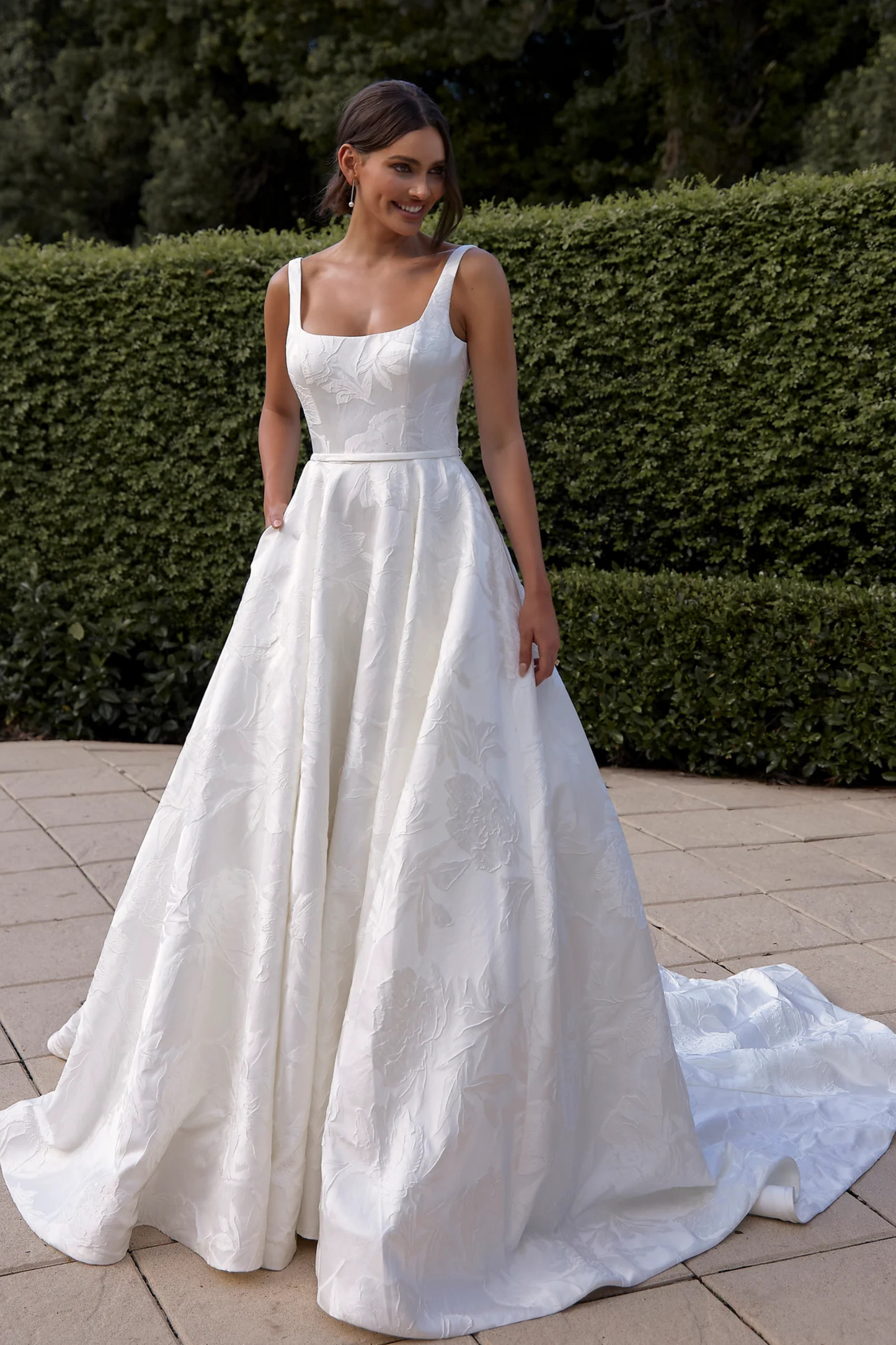 Woman in a white wedding dress standing outdoors with greenery in the background