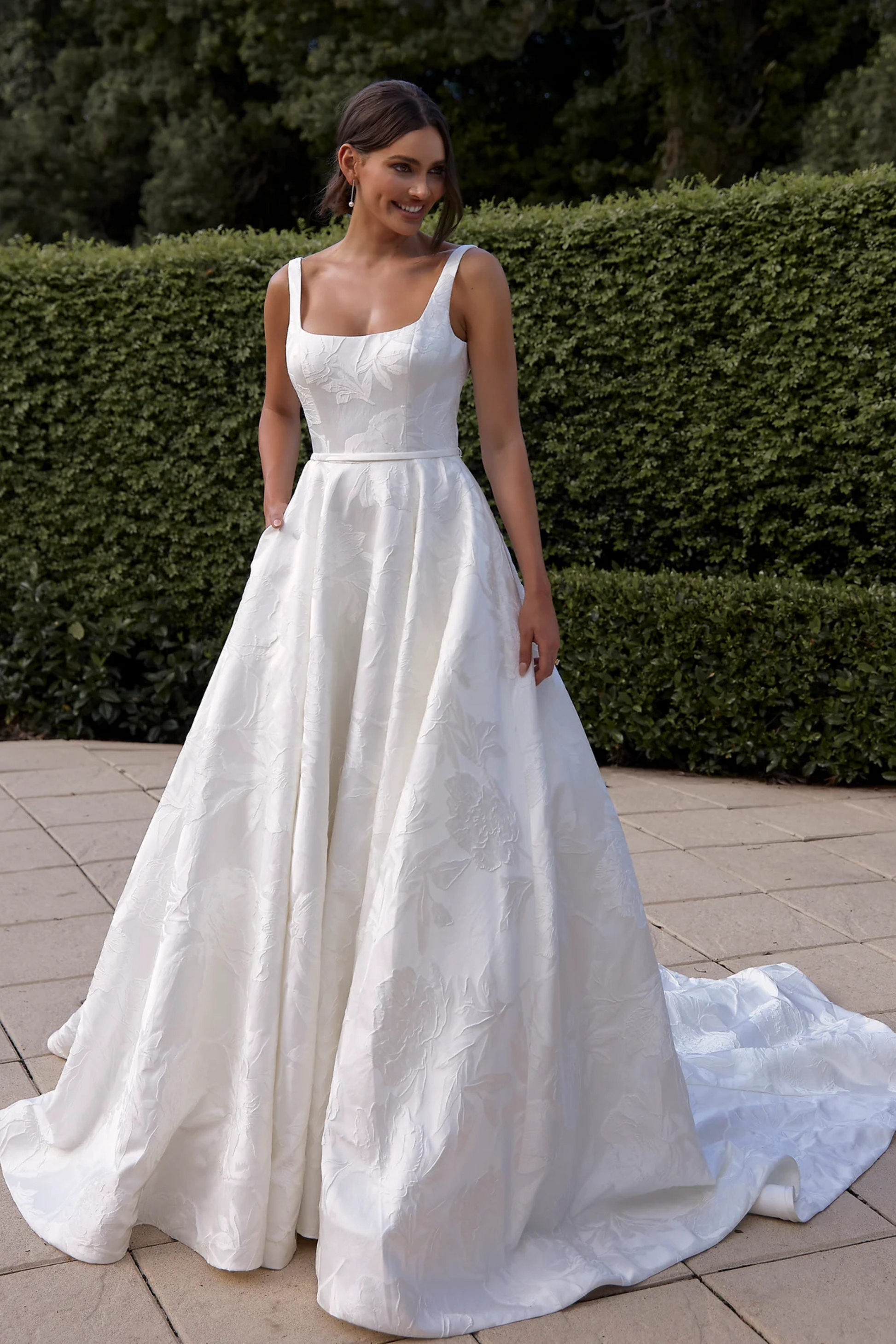 Woman in a white wedding dress standing outdoors with greenery in the background
