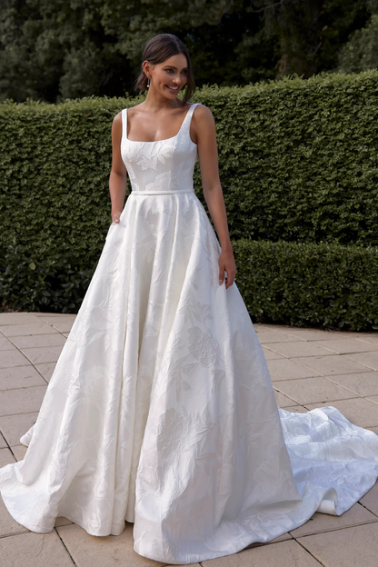 Woman in a white wedding dress standing outdoors with greenery in the background