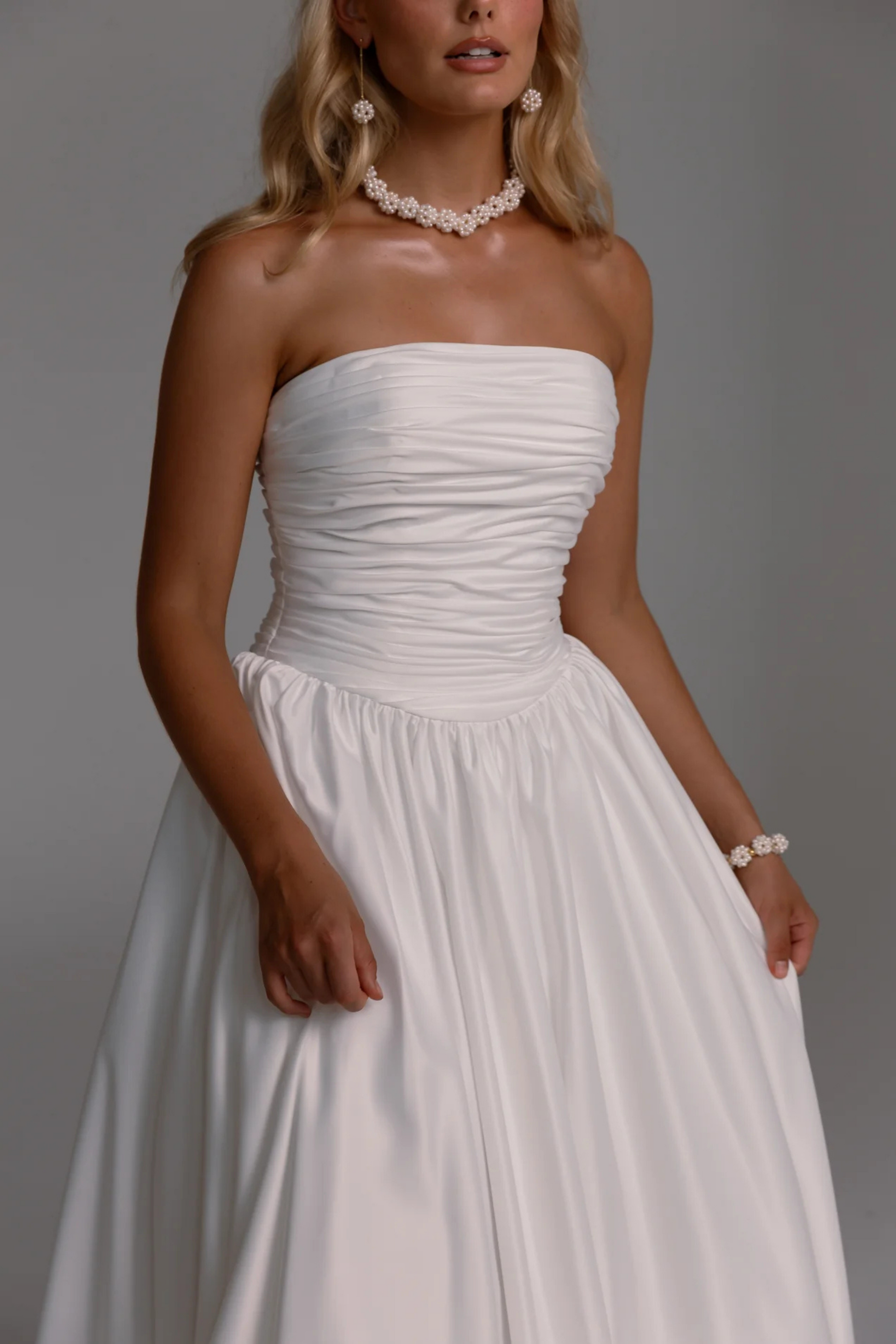 Woman wearing a strapless white dress with pearl jewelry against a gray background