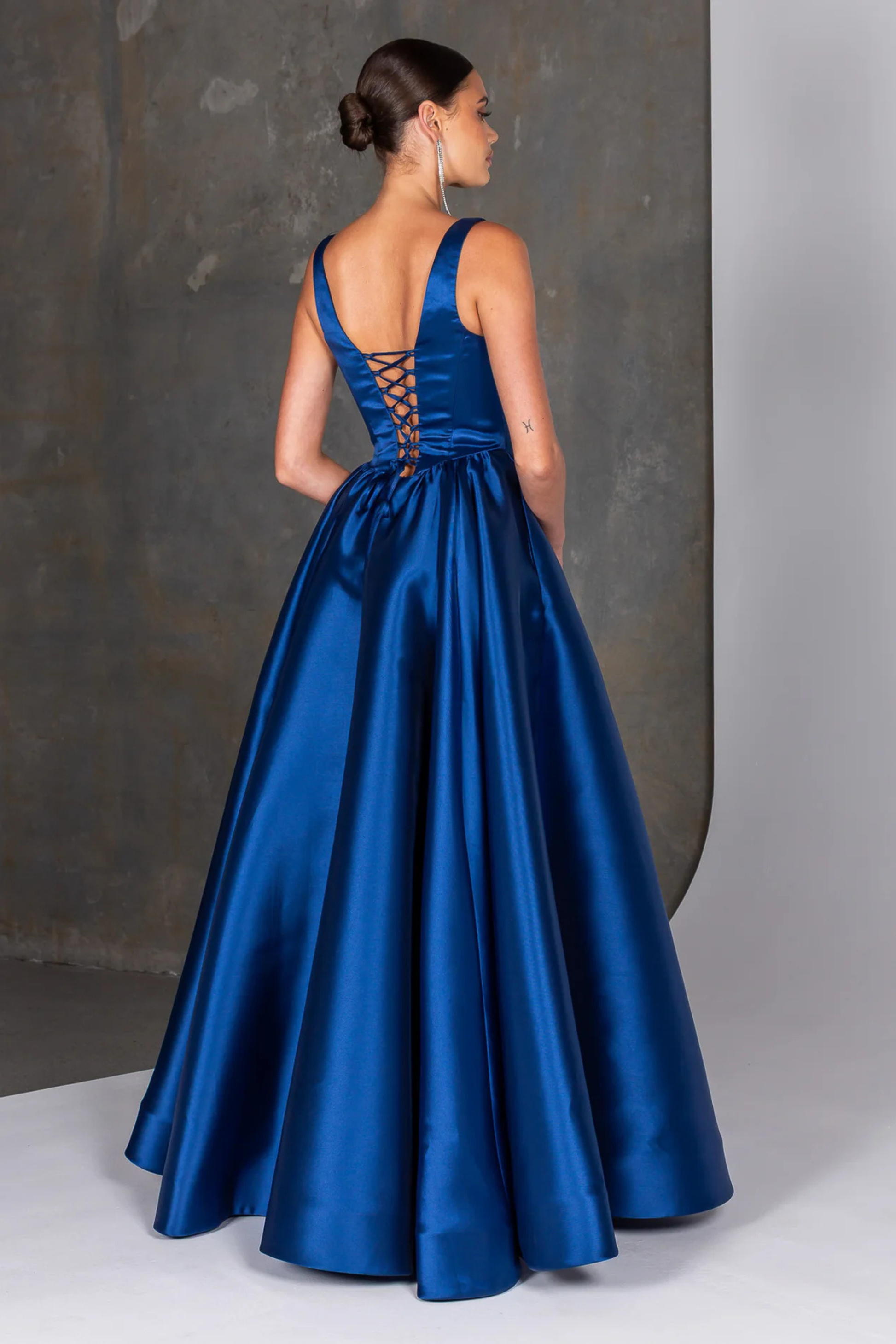 Woman wearing a navy evening gown with a lace-up back against a neutral background