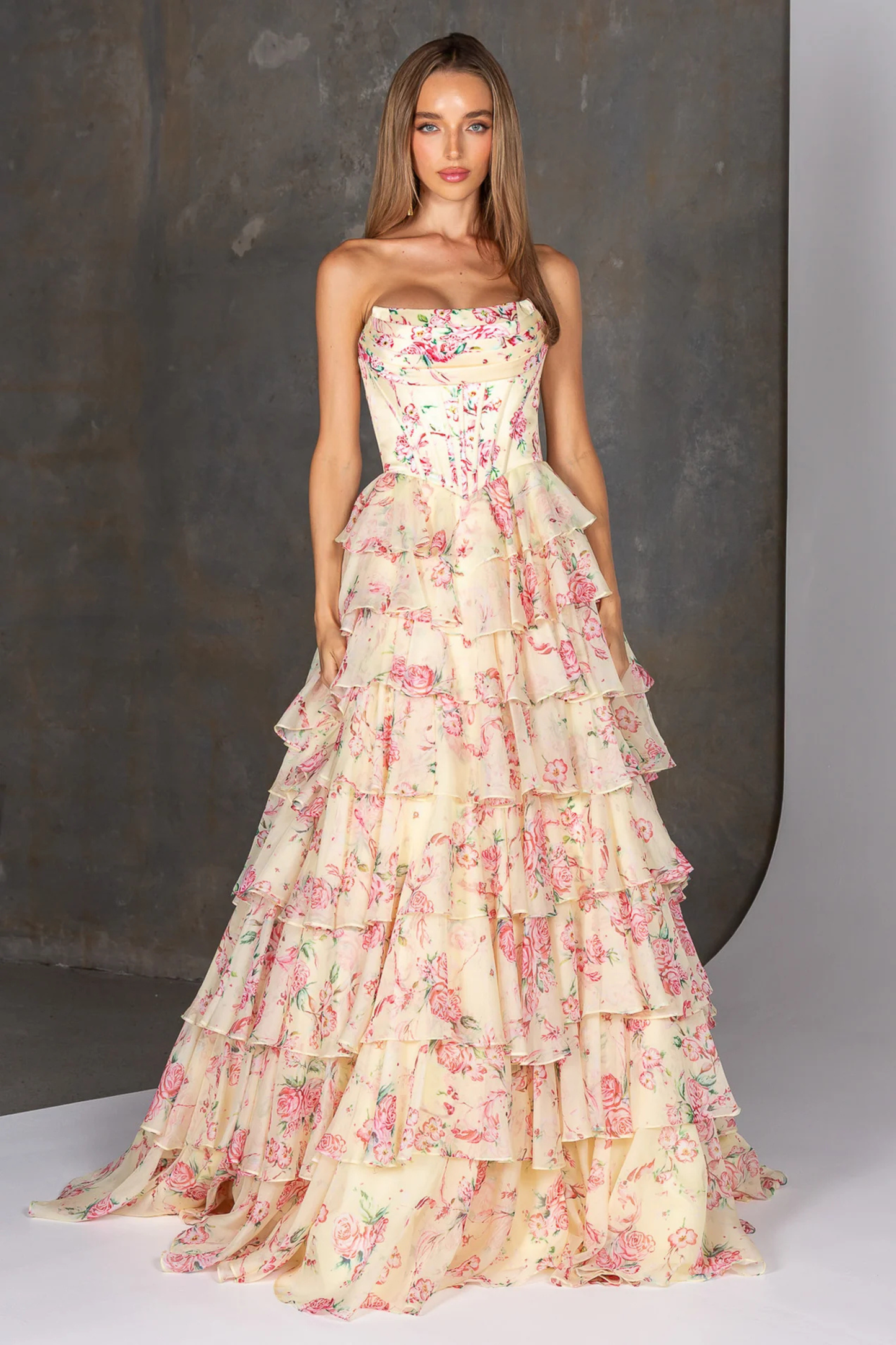 Woman wearing a strapless yellow floral gown with ruffled layers against a neutral background