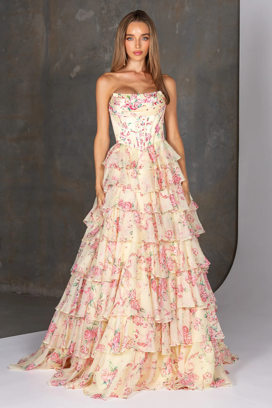 Woman wearing a strapless yellow floral gown with ruffled layers against a neutral background
