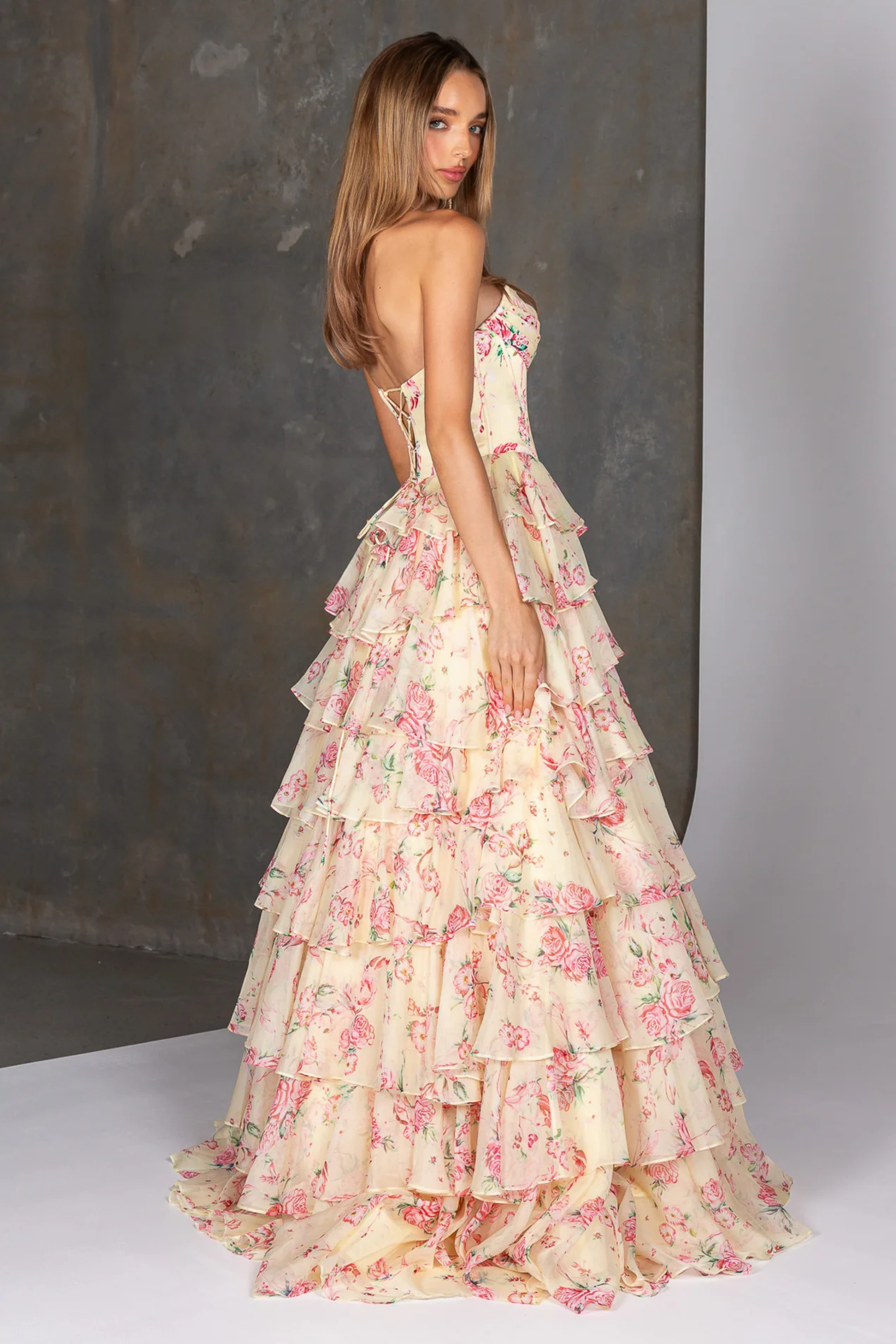 Woman wearing a yellow floral dress with a plain background showing the back of the dress