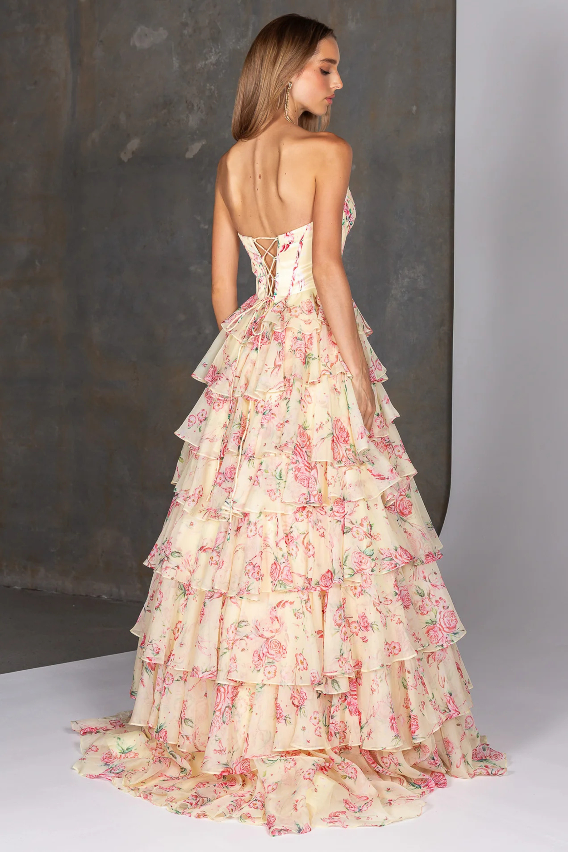 Woman wearing a yellow floral dress with a gray background showing the back of the dress design