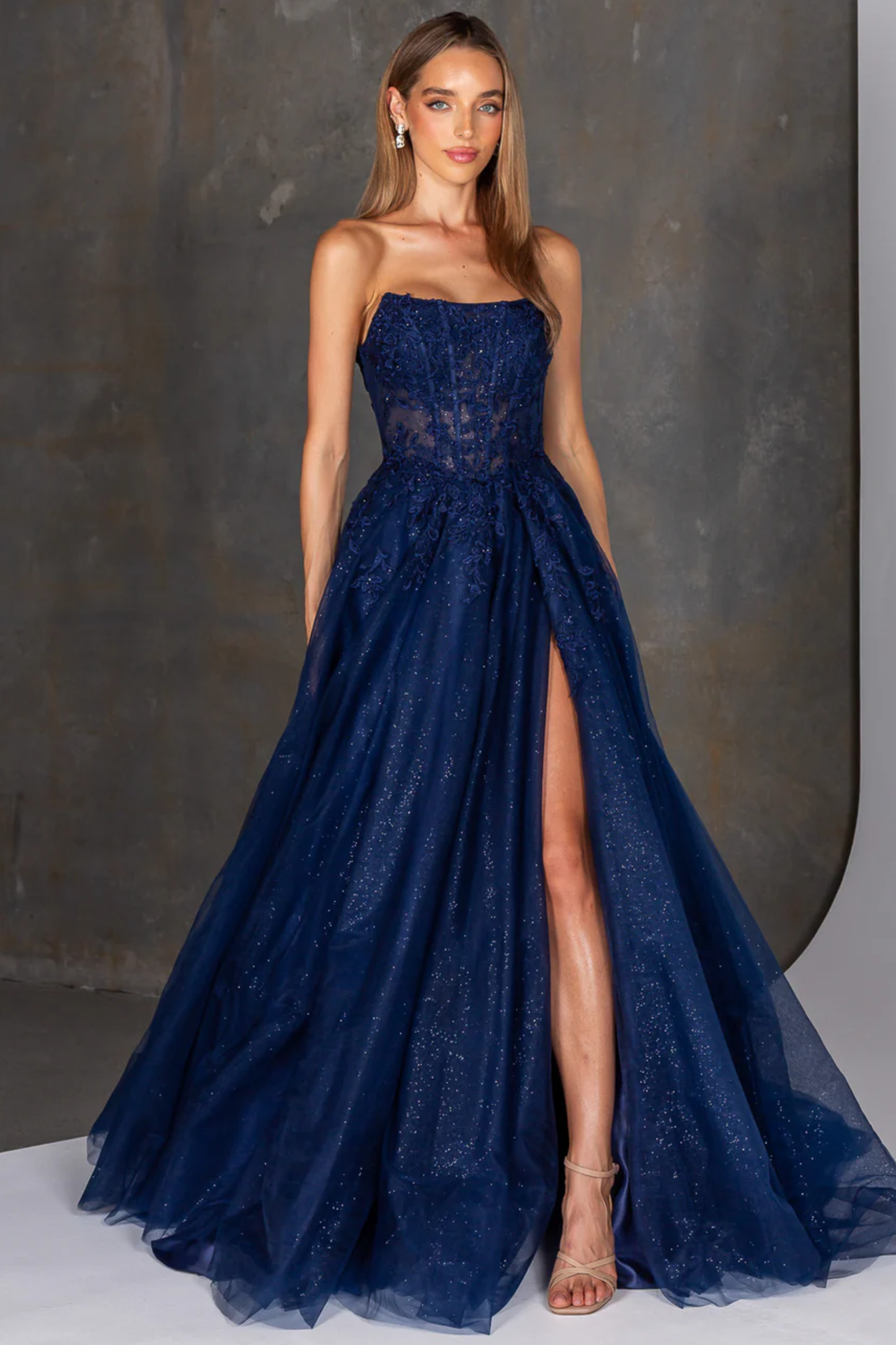 Woman wearing a navy blue strapless gown with a slit on a neutral background