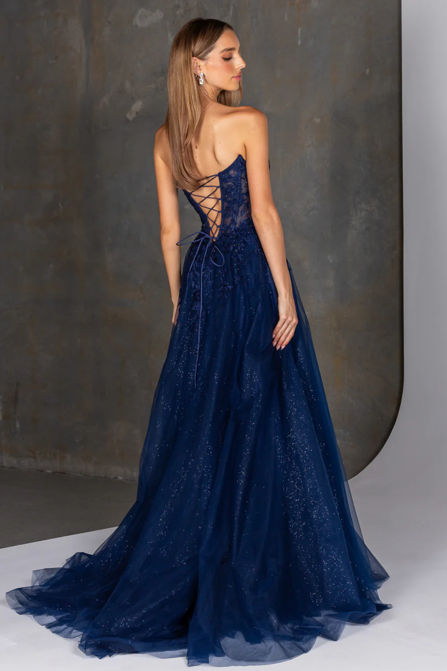 Navy blue lace evening gown with a backless design on a neutral background