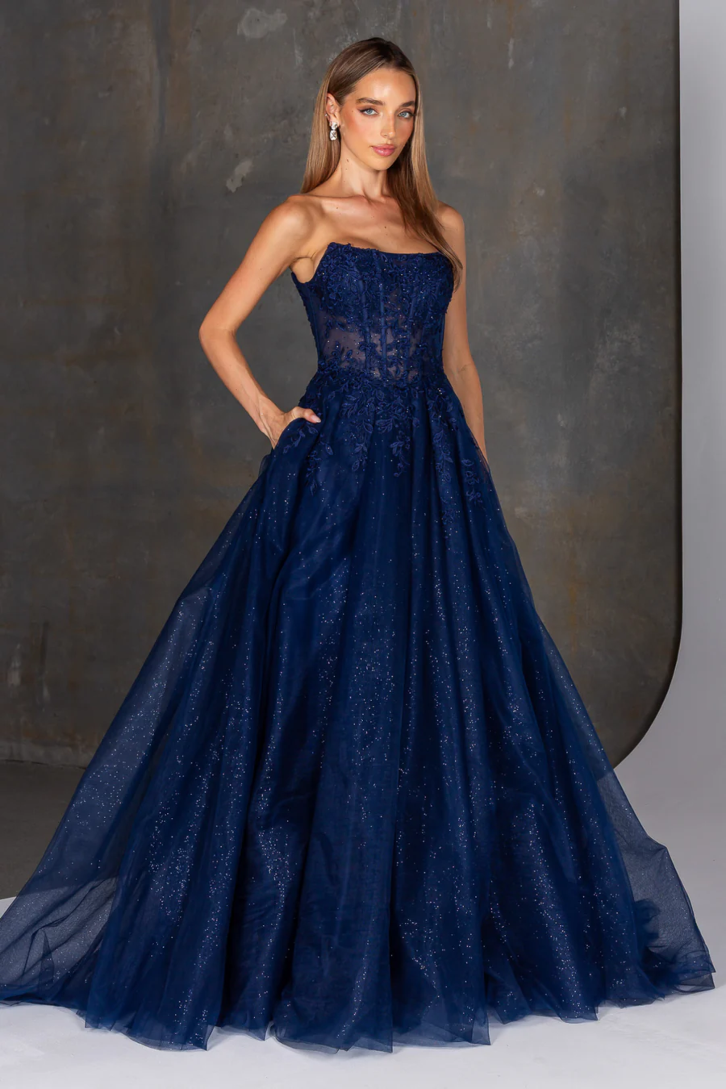 Woman wearing a navy blue strapless gown against a dark background