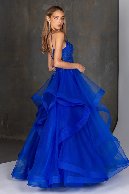 Royal blue evening gown featuring a fitted embellished bodice with delicate beading and thin spaghetti straps, flowing into a dramatic multi-layered tulle skirt with soft cascading ruffles. A statement formal dress ideal for prom, gala, or special occasion wear, showcasing elegant movement and a bold, vibrant color. Showing the side design of the gown.