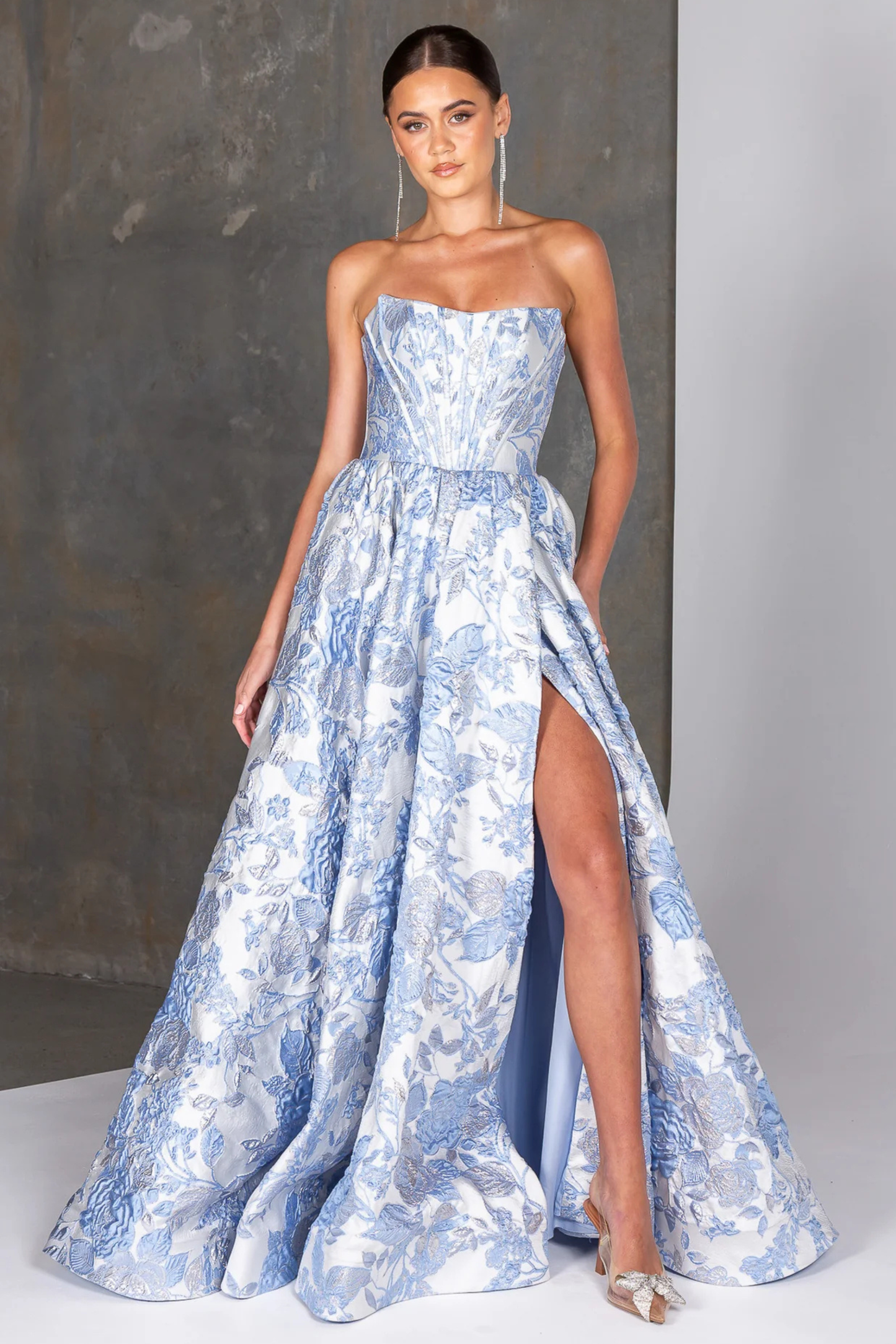 Woman wearing a strapless blue floral gown with a high slit on a plain background
