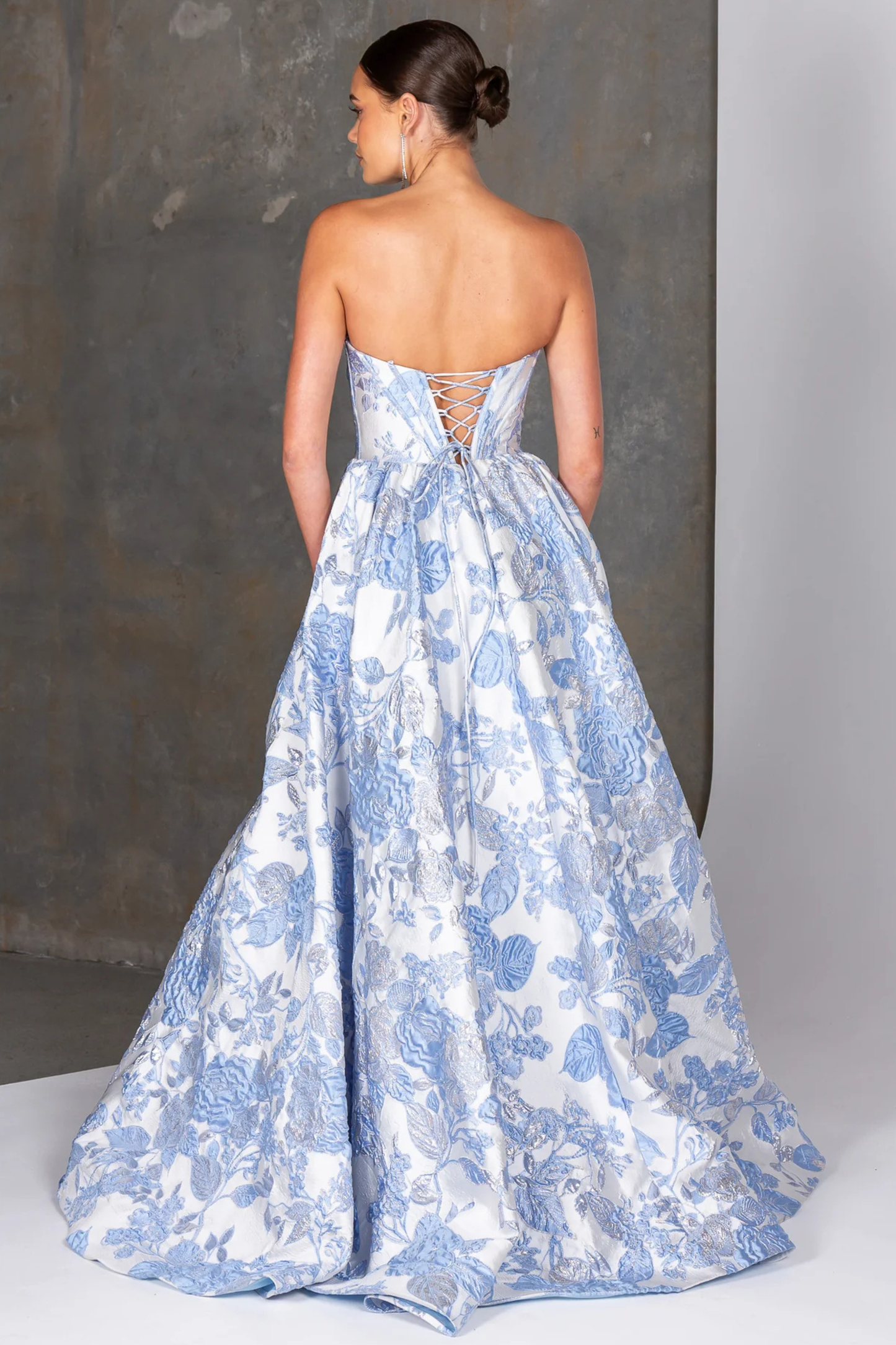 Woman wearing a blue floral strapless gown against a gray background