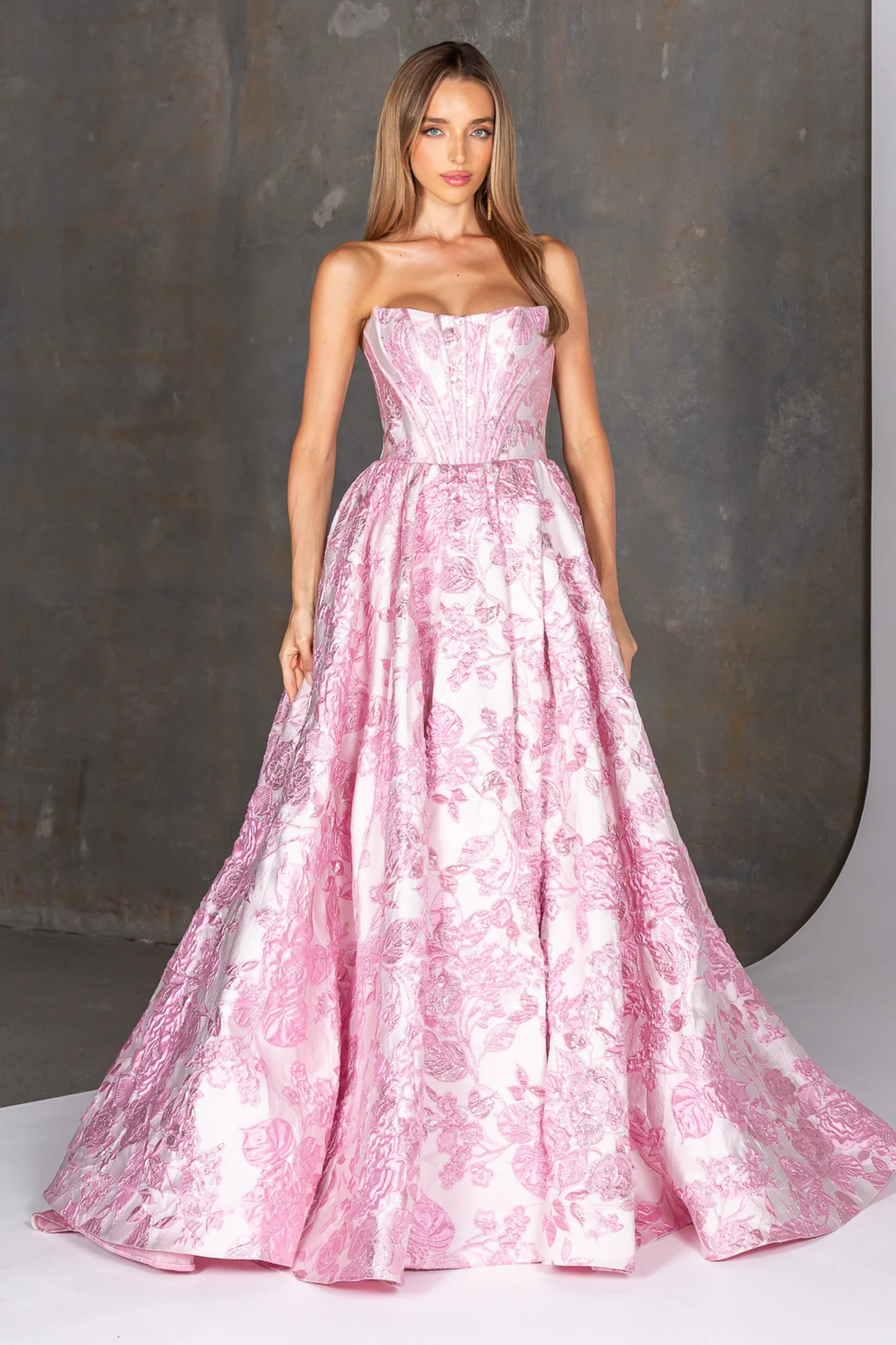 Woman wearing a pink strapless gown with floral pattern against a gray background