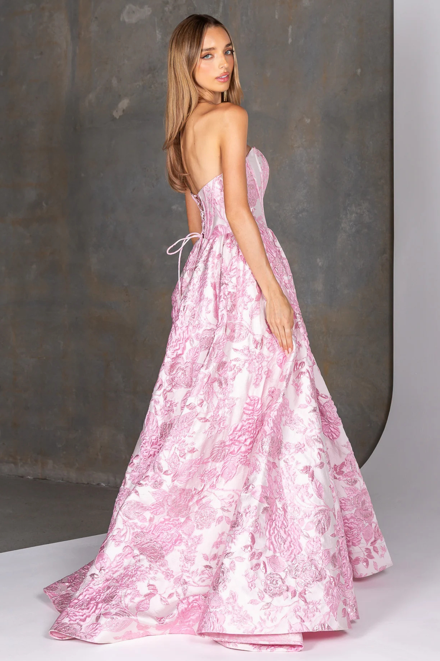 Woman wearing a pink floral strapless gown against a neutral background