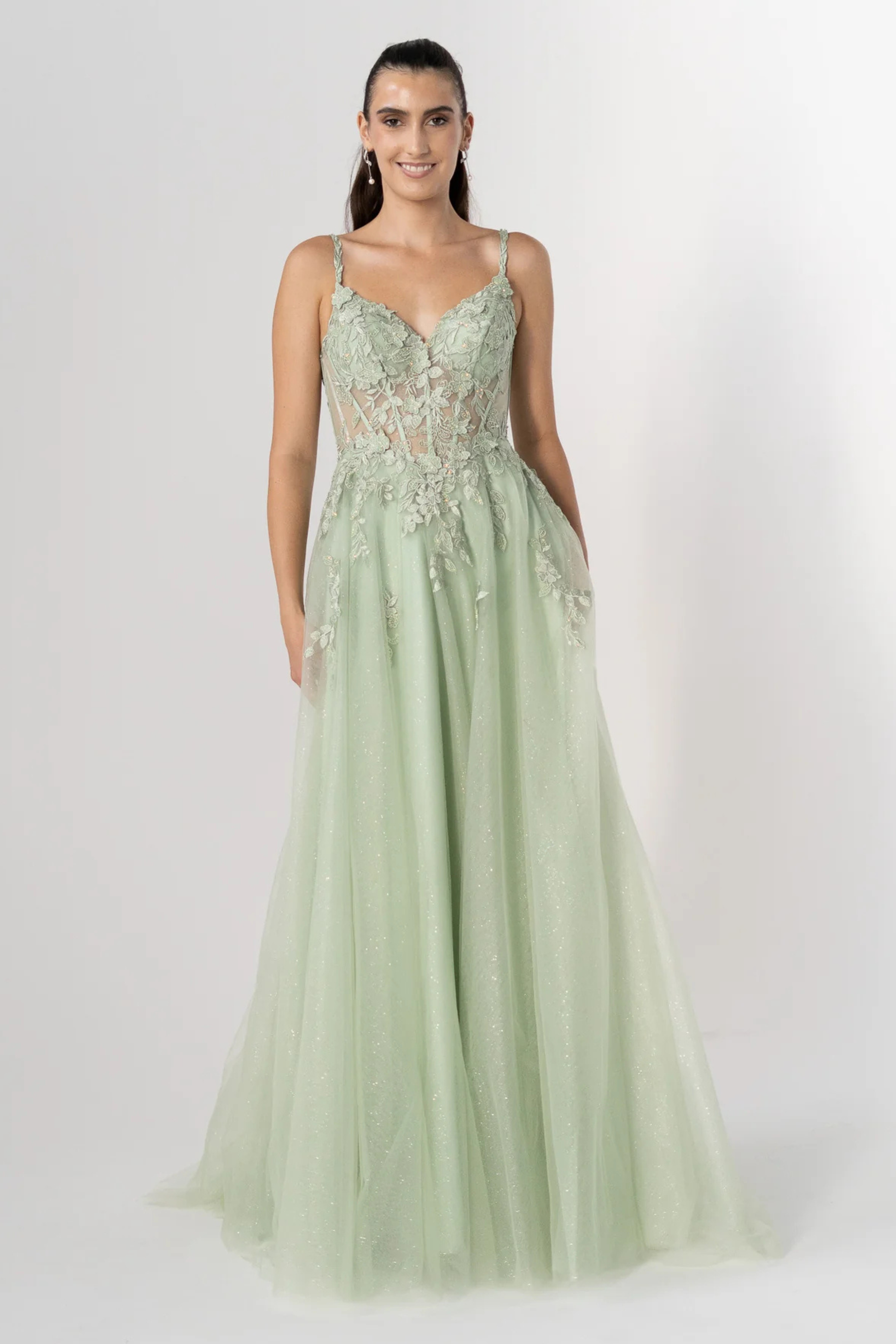 Woman wearing a light green evening gown with lace details on a white background
