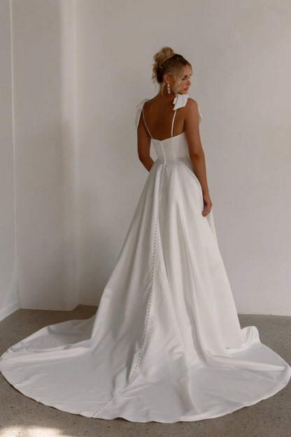 Tania Olsen Designs Anne wedding dress in vintage white featuring a square neckline, detachable bow straps, satin A-line skirt and chapel-length train with buttons.